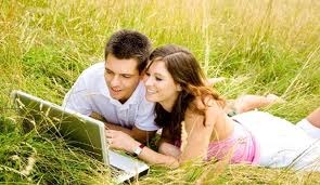giovane coppia distesa su di un prato mentre consula il computer